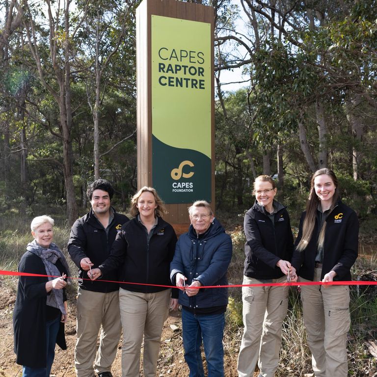 Founder Phil Pain and Capes Raptor Centre staff cutting a red ribbon in front of a new Capes Raptor Centre sign.
