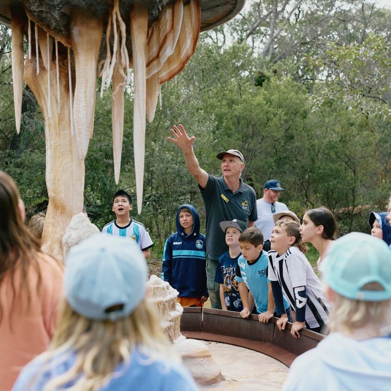 Tour guide with a school group pointing at life-sized replicas of cave formations along the above-ground Ancient Lands Experience at Ngilgi Cave.