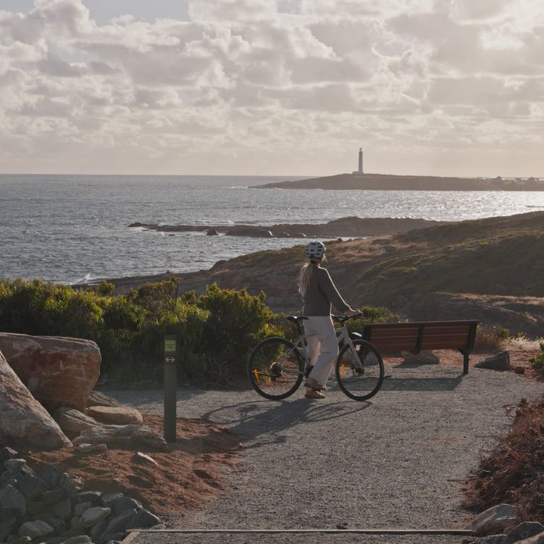 Along the Leeuwin-Biddi Trail, a bike rider pauses to admire the view of the coastline and the Cape Leeuwin Lighthouse