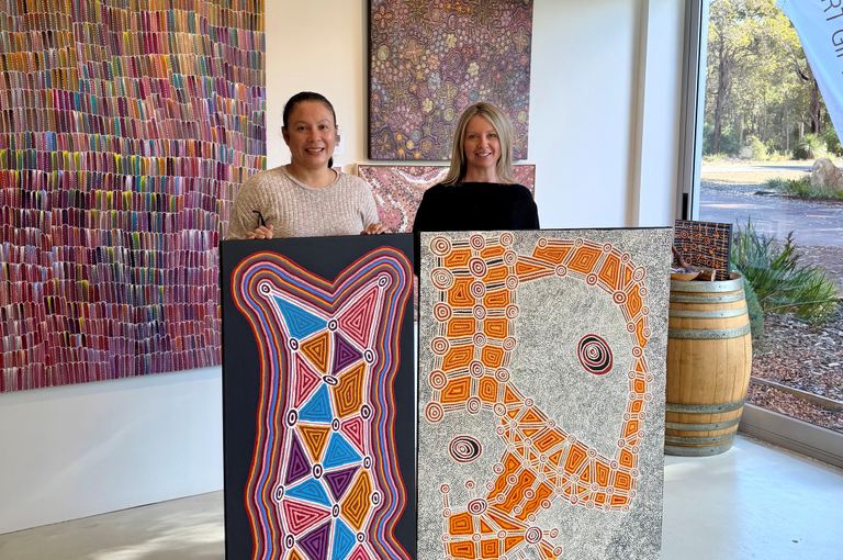 2 woman holding up 2 aboriginal artworks in a gallery