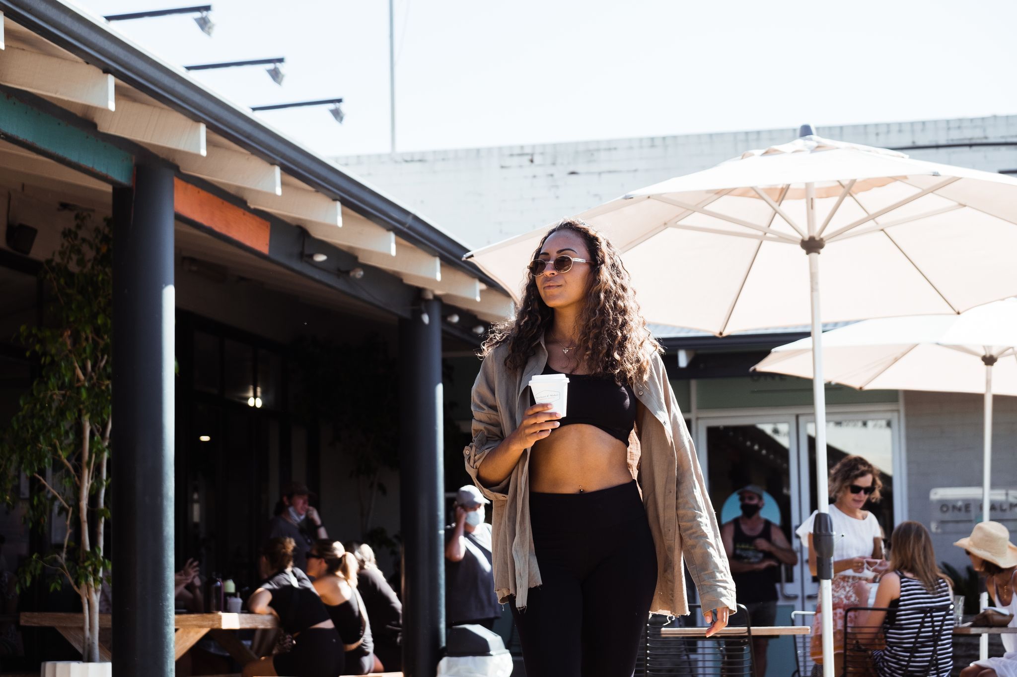 Person walking outside a cafe holding a coffee cup, wearing active wear. Credit Rachel Claire.