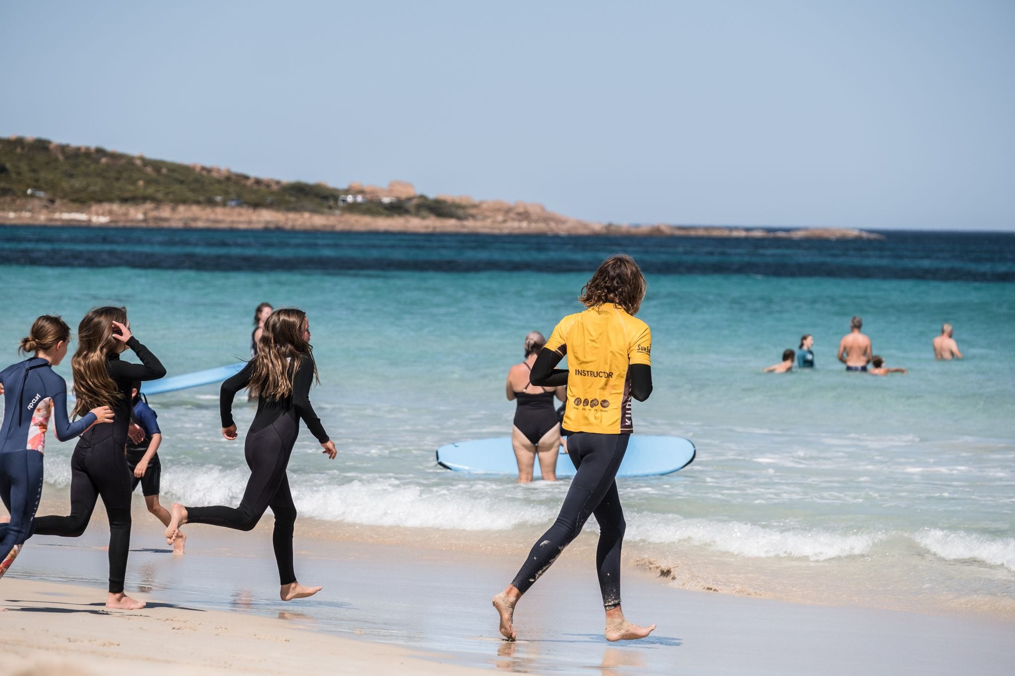 Group of kids in wetsuits running into the water to learn how to surf. Credit Rachel Claire.