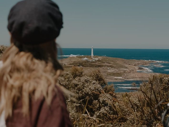 Back of person looking out to Cape Leeuwin Lighthouse in the distance, on a sunny day. Credit Jarrad Seng (Drive Your Story)