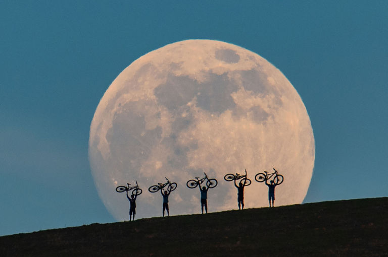 image f a moon with 5 silhouettes of bike riders in front of it holding bikes into the air