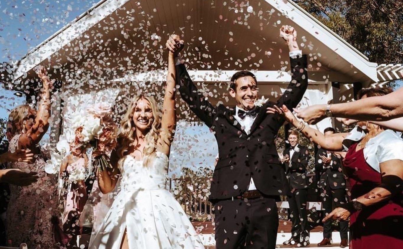 Married couple walking through confetti surrounded by wedding guests
