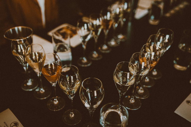 Close up image of three rows of wine glasses lined up on a table with a dark coloured table cloth