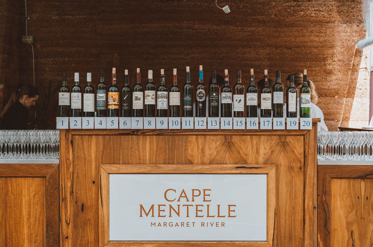 A wooden counter with the sign 'cape mentelle' on its front, with a row of wines sitting across the length of it