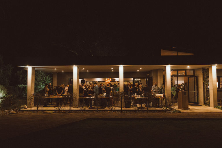 Long shot of a restaurant front featuring a deck with tables and people standing behind them