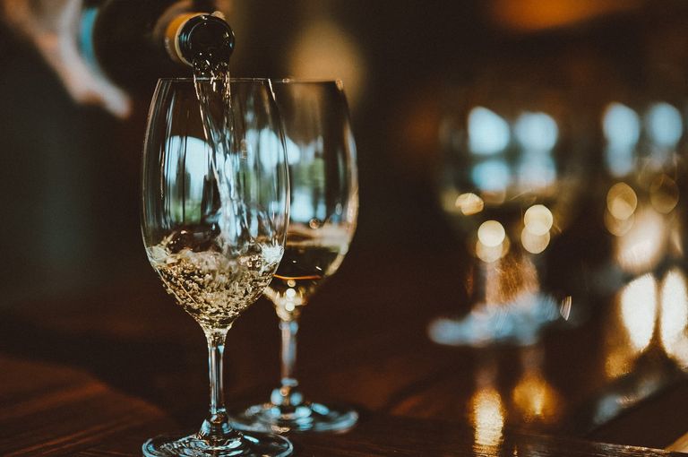 Close up of two glasses of wine with white wine being poured in each