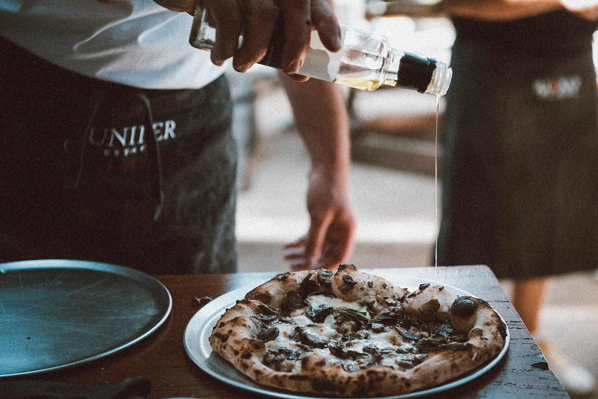 Close up image of a chef pouring olive oil over a pizza