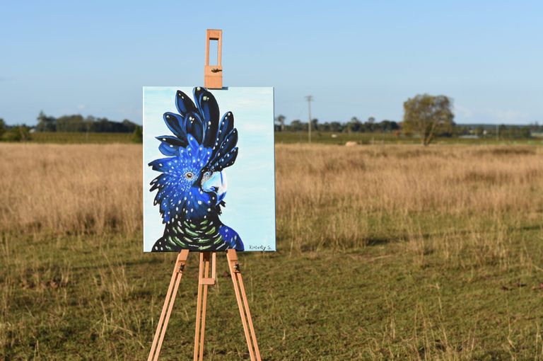 Canvas with a painted cockatoo placed outside on a field