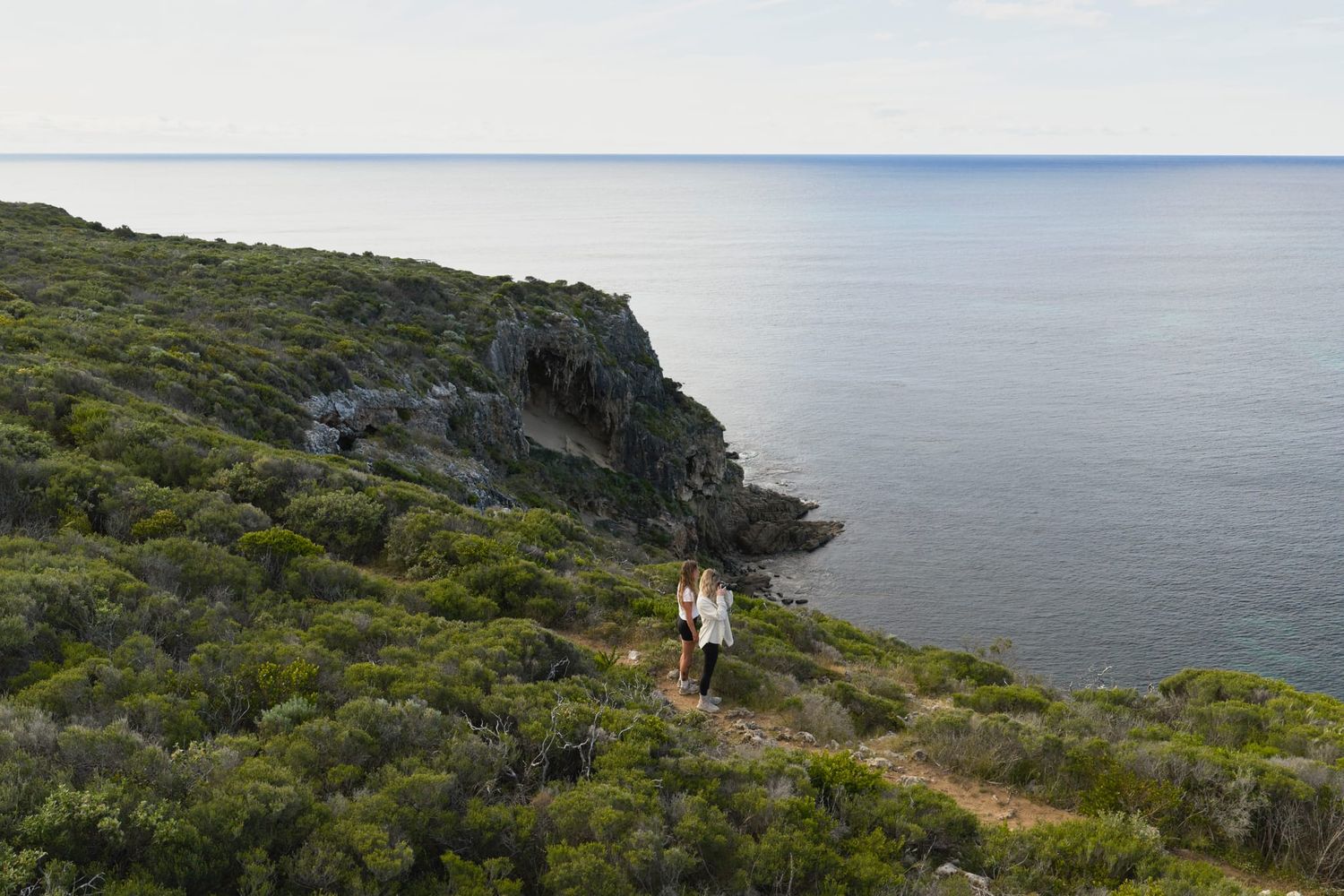 Two people enjoying the view around Cape Naturaliste with ancient karst formation and ocean in the background.