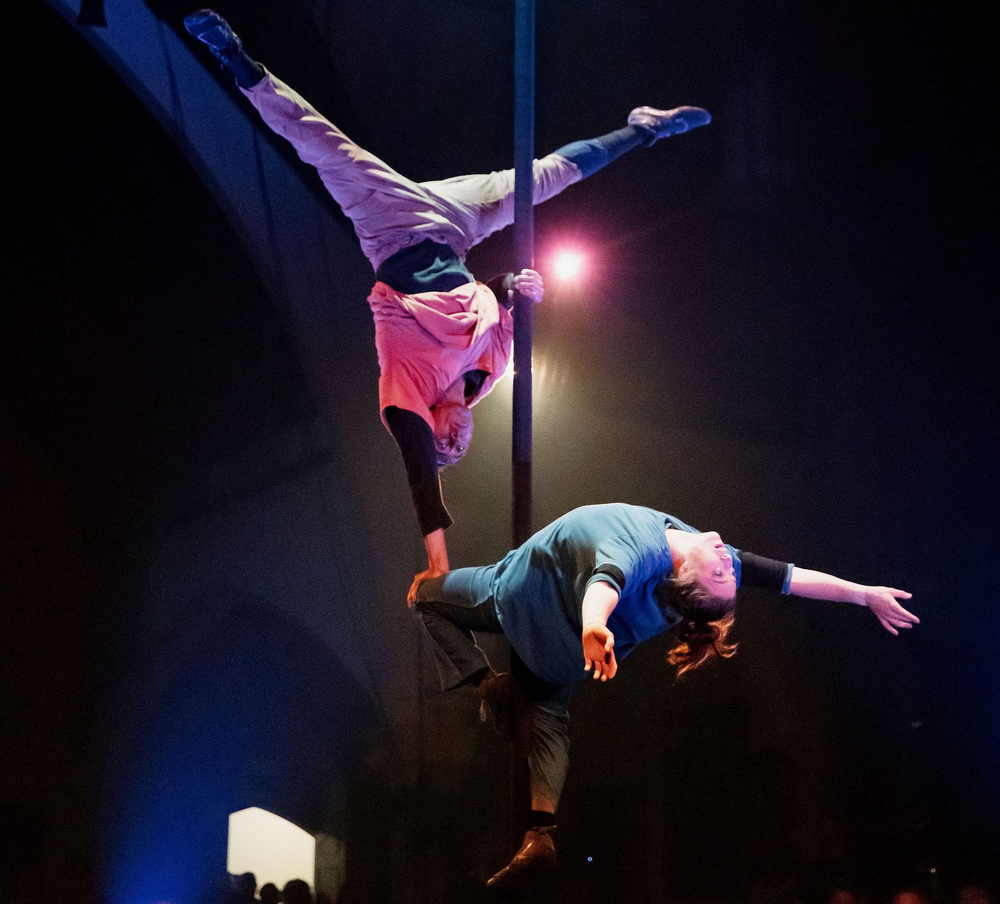 Circus performers performing tricks on a long metal pole high above the ground