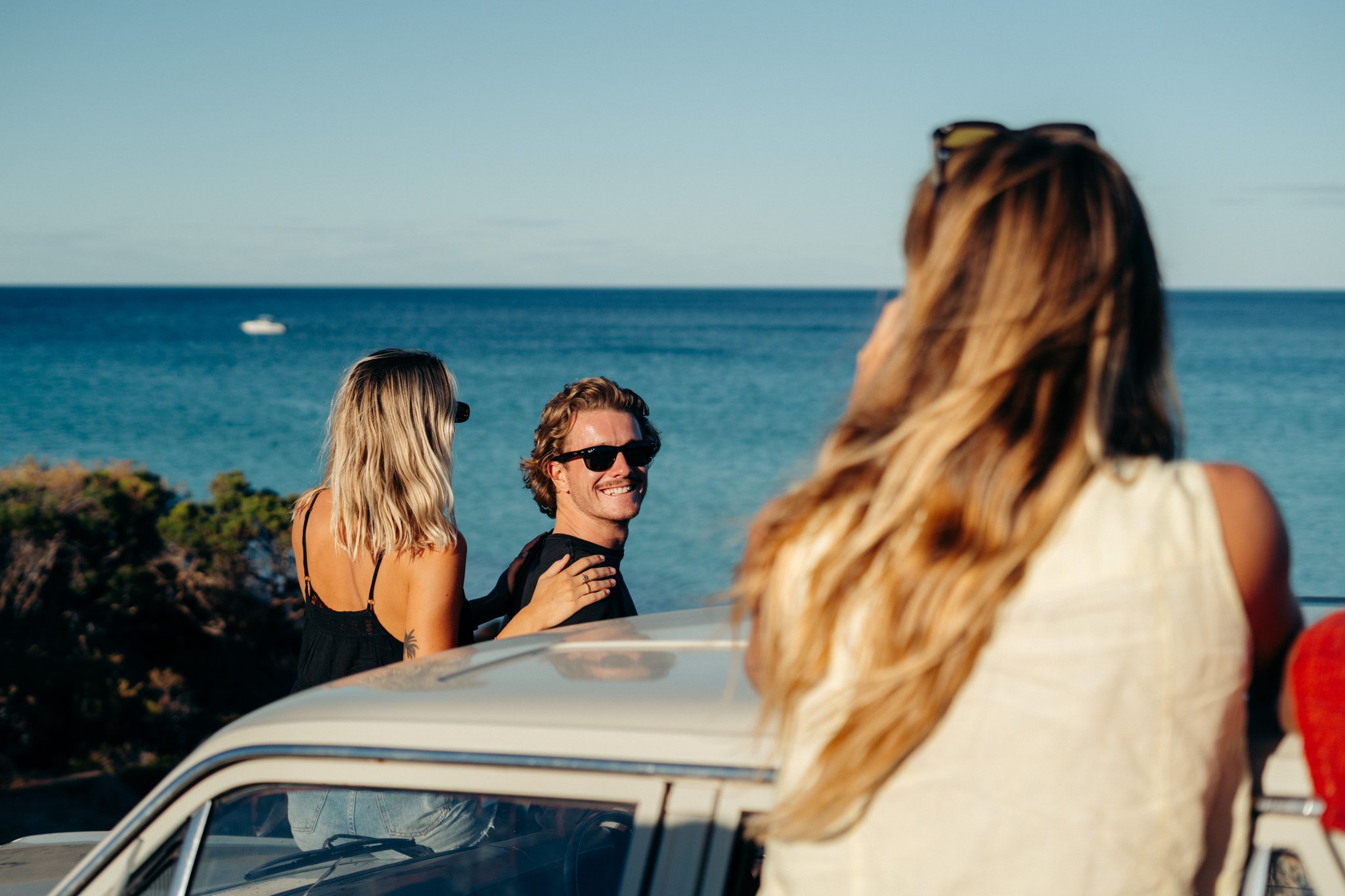 People near a car smiling with the ocean in the background