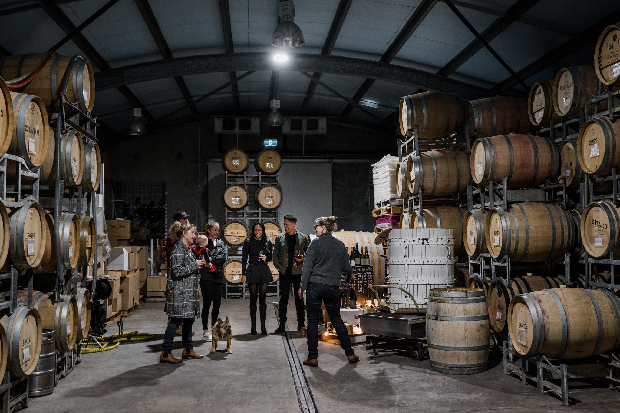 People inside a cellar door with wine barrels discussing wine making methods