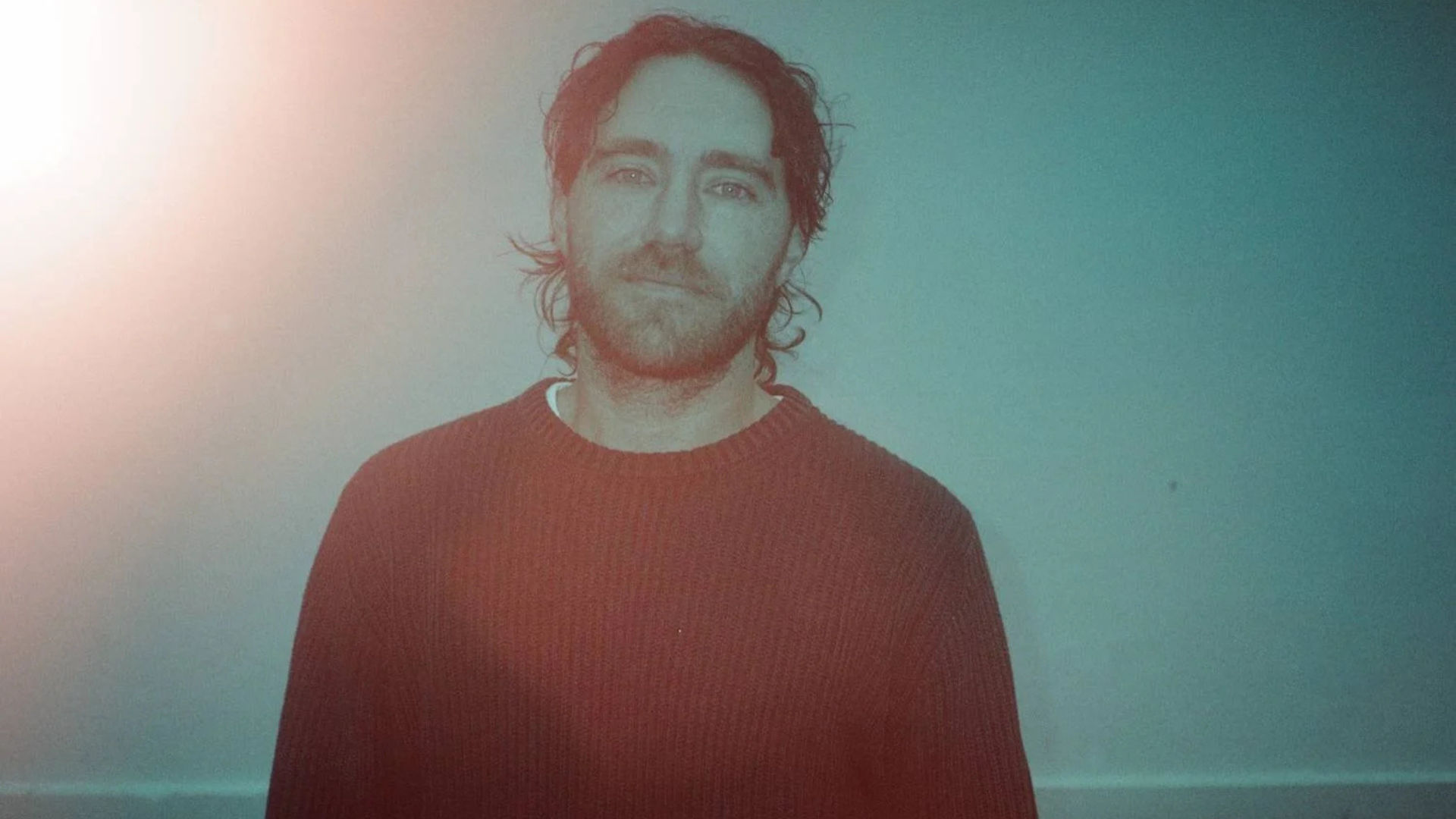 Australian musician Matt Corby smiling in front of tinted background.