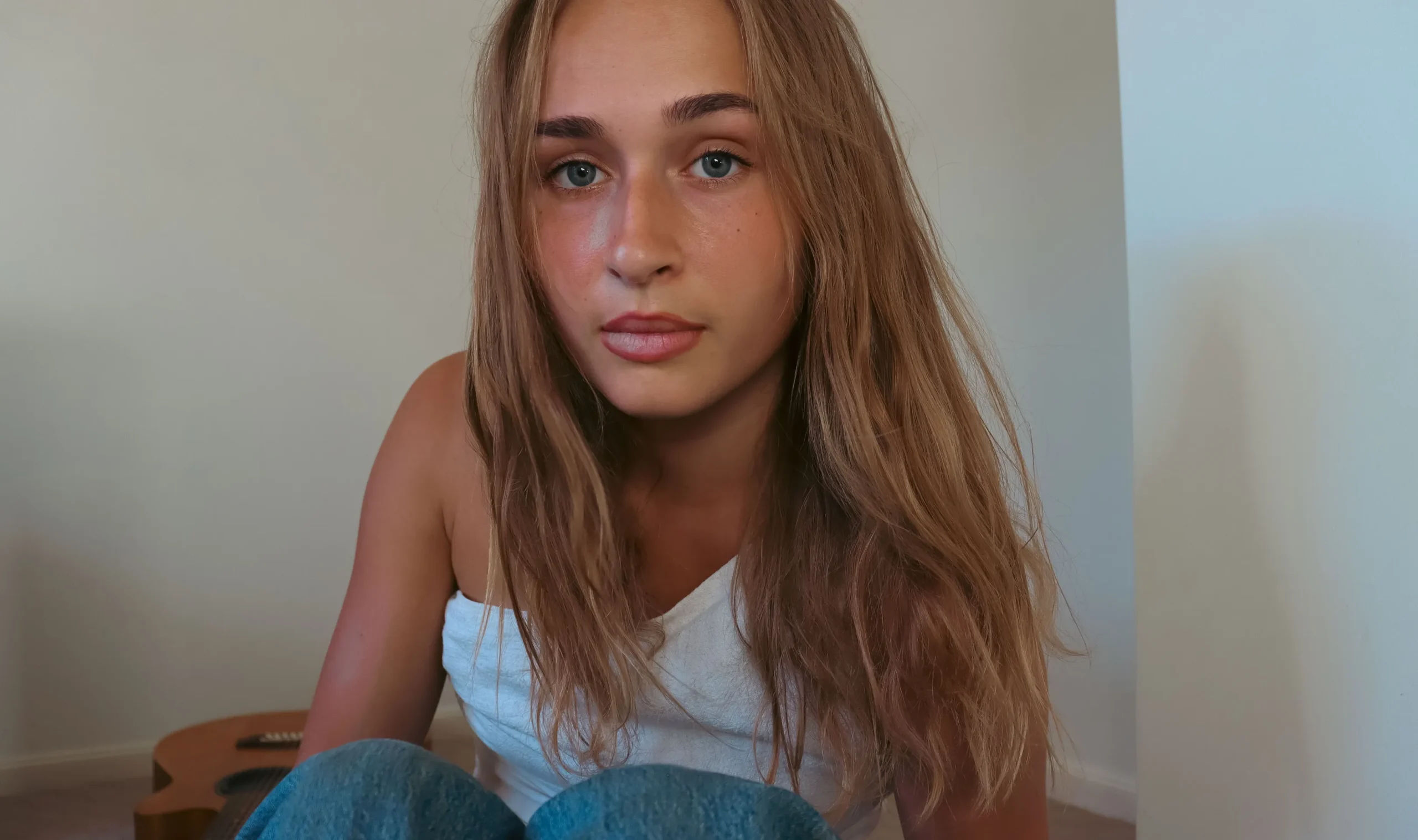 Madi Goodwin sitting on the floor beside her guitar.